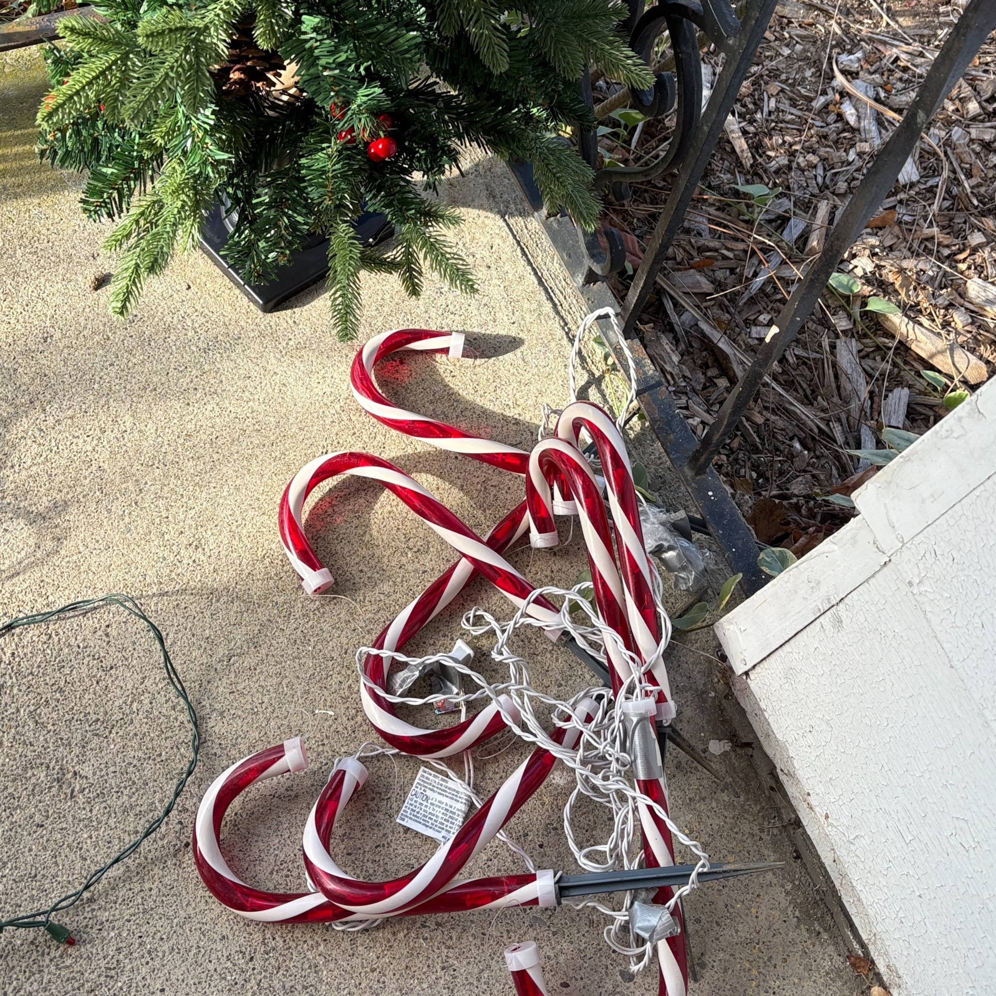 Image of a partially visible fake outdoor chrismas tree on a stoop with candy cane lights in a pile 